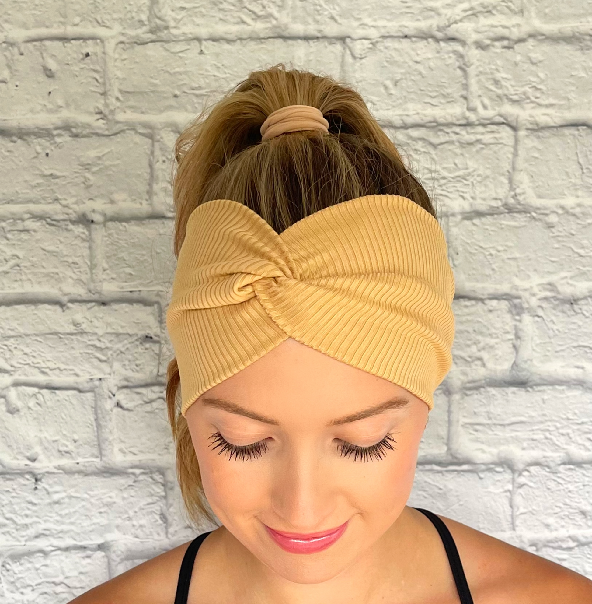 Woman with hair in ponytail wearing wide, twisted headband with tan ribbed fabric.