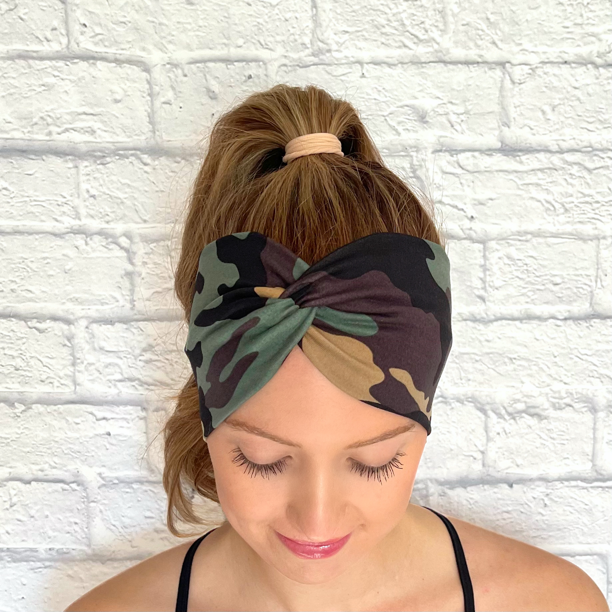 Woman with hair in curled ponytail wearing wide, twisted headband in camo print.