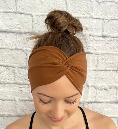 Woman with hair in bun wearing wide, twisted headband in caramel color.