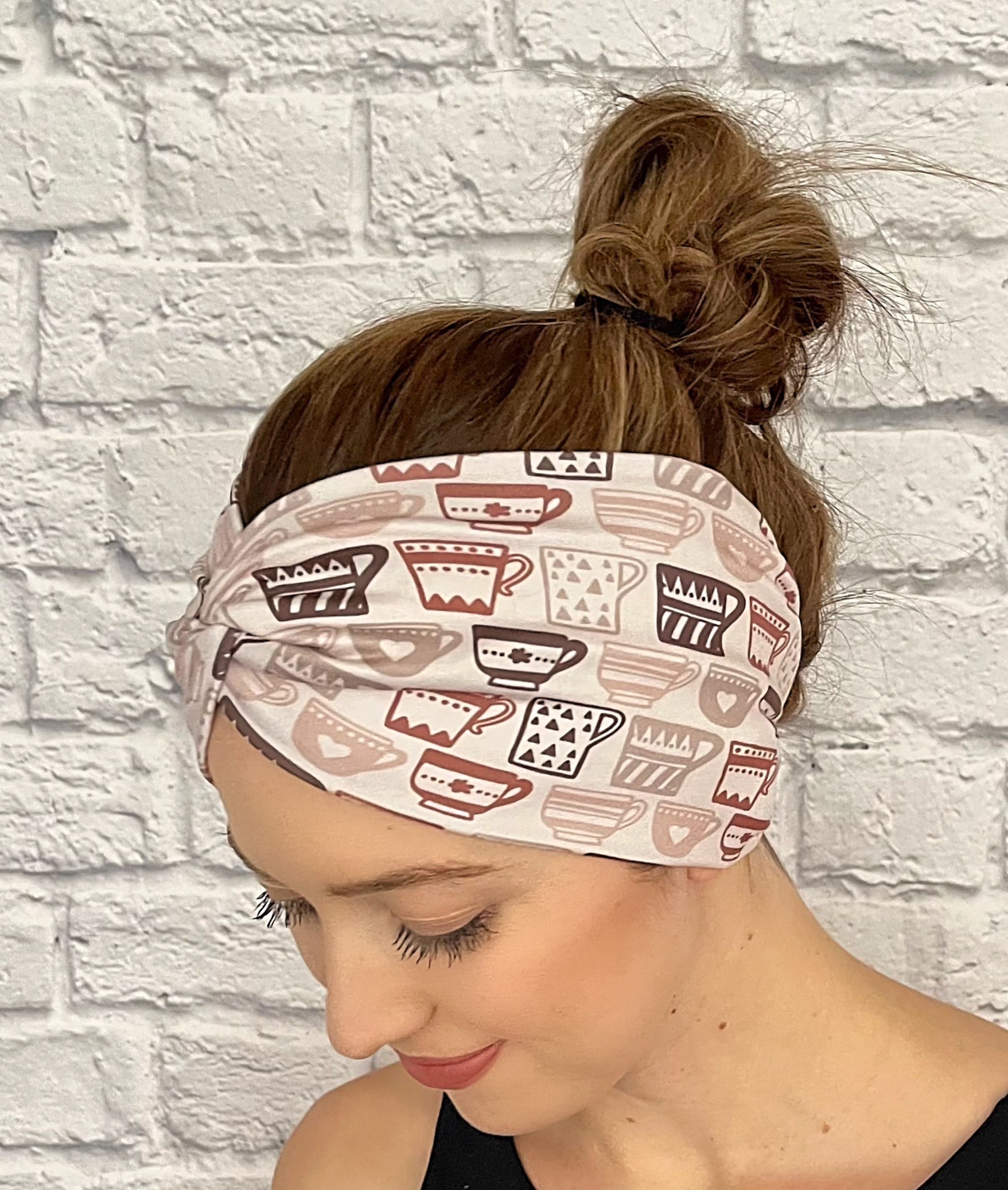 Woman with hair in bun wearing wide, twisted headband in light brown with brown coffee cup print.