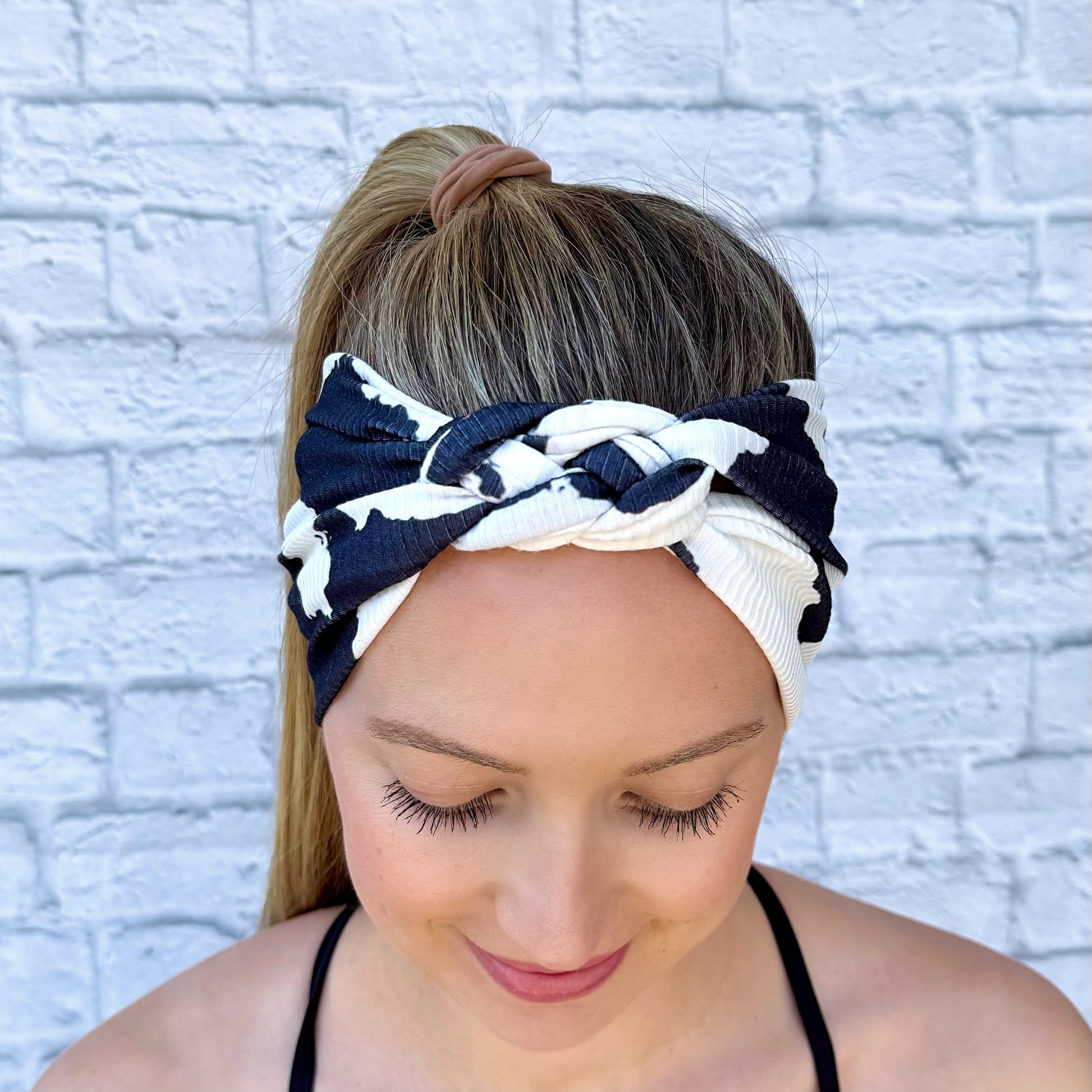 Woman with hair in ponytail wearing black and white cow print headband in sailor knot style with ribbed fabric.