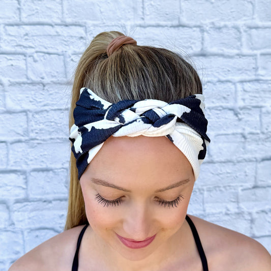 Woman with hair in ponytail wearing black and white cow print headband in sailor knot style with ribbed fabric.