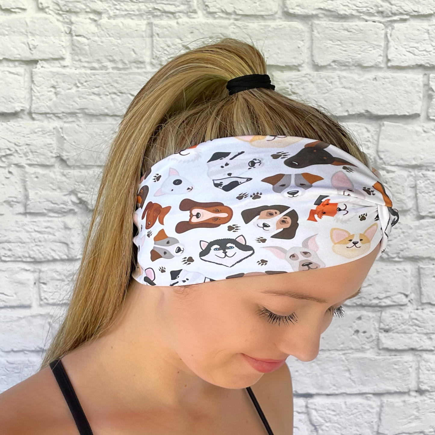 Woman with hair in ponytail wearing white, wide twisted headband with dog theme print.