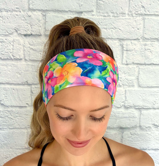 Woman with hair in ponytail wearing flat, stretchy headband in blue with bright, multi-color Hawaiian theme floral print.