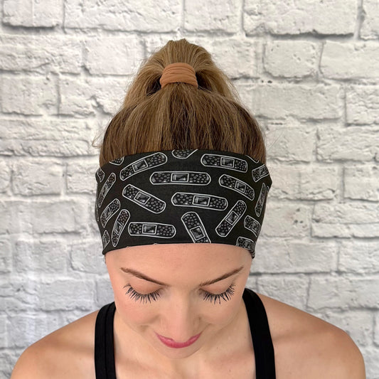 Woman with hair in bun wearing flat, stretchy headband in black with white bandage print.