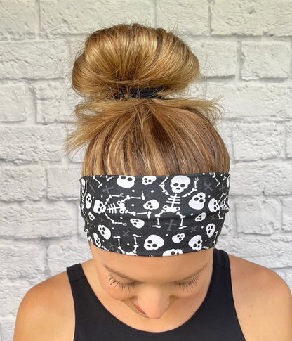 Person wearing a black headband with white skull and skeleton designs against a light gray brick wall.