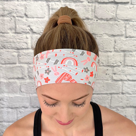Woman with hair in curled ponytail wearing light blue/gray headband with "PT" print in orange and PT theme print with flowers in dark gray/blue and orange.