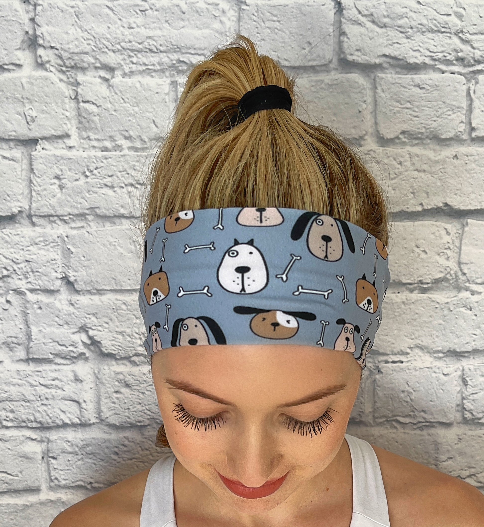 Woman with hair in ponytail wearing flat, stretchy, blue headband with dog theme print.