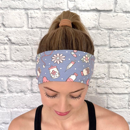 Woman with hair in ponytail wearing flat, stretchy headband in blue with pink, white, and mint color medical theme print.