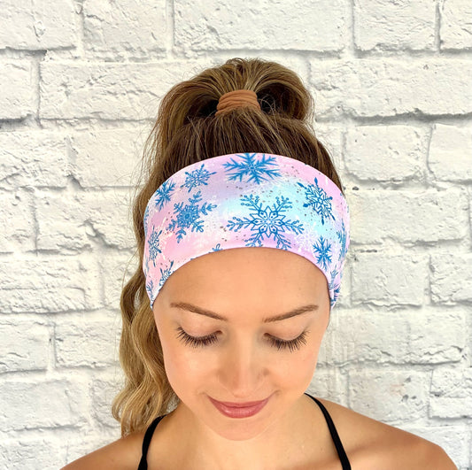 Woman wearing a colorful headband with snowflake pattern against a white brick wall.