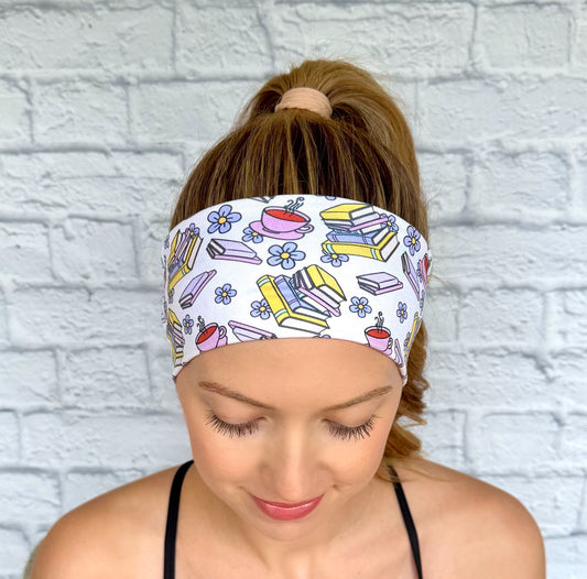Woman with hair in ponytail wearing flat, stretchy, white headband with book, flower, and coffee print.