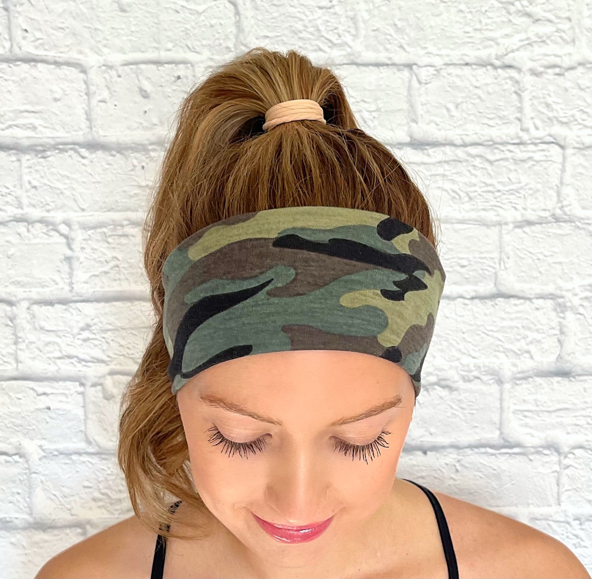 Woman with hair in curled ponytail wearing flat, stretchy headband with green and black camo print.