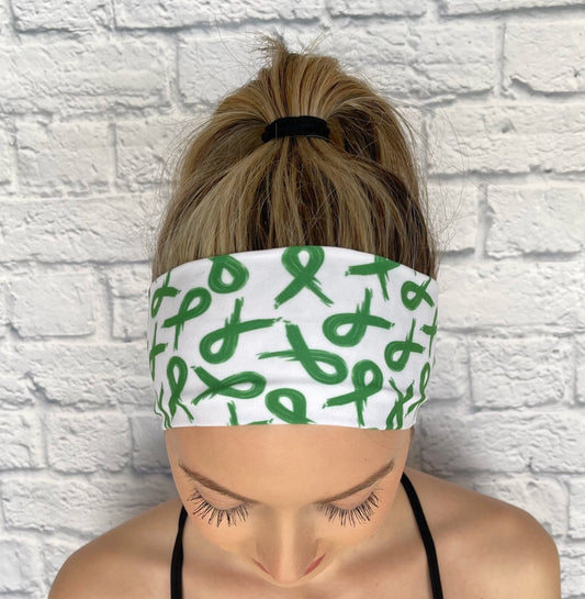 Woman with hair in ponytail wearing flat, stretchy headband in white with green ribbon print.