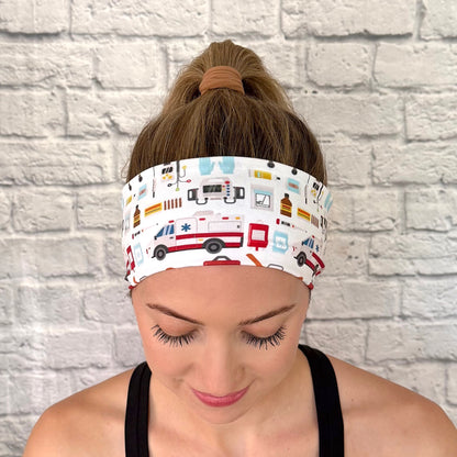 Woman with hair in bun wearing flat, stretchy, white headband with EMT and ambulance theme print.