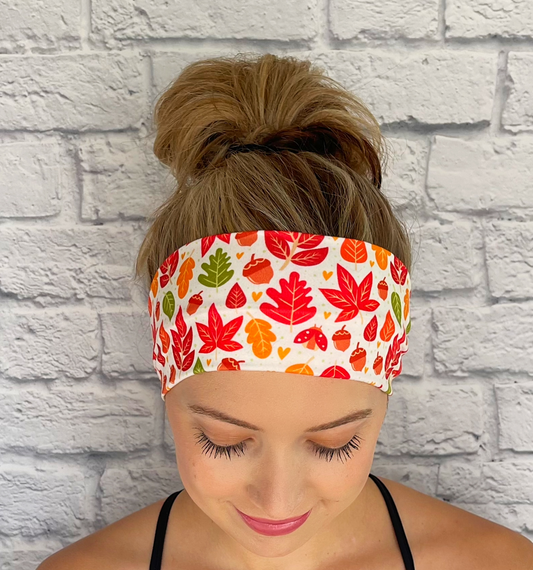 Woman with hair in bun wearing flat, stretchy, white headband with orange, red, and green fall leaves print.