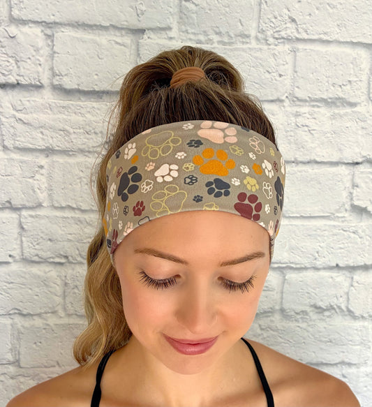 Woman with hair in ponytail wearing flat, stretchy, green headband with multi-color dog paw print.