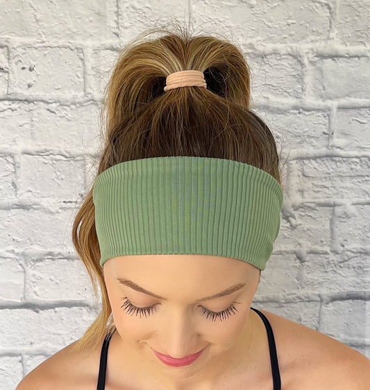Woman with hair in ponytail wearing flat, stretchy headband in green ribbed fabric.