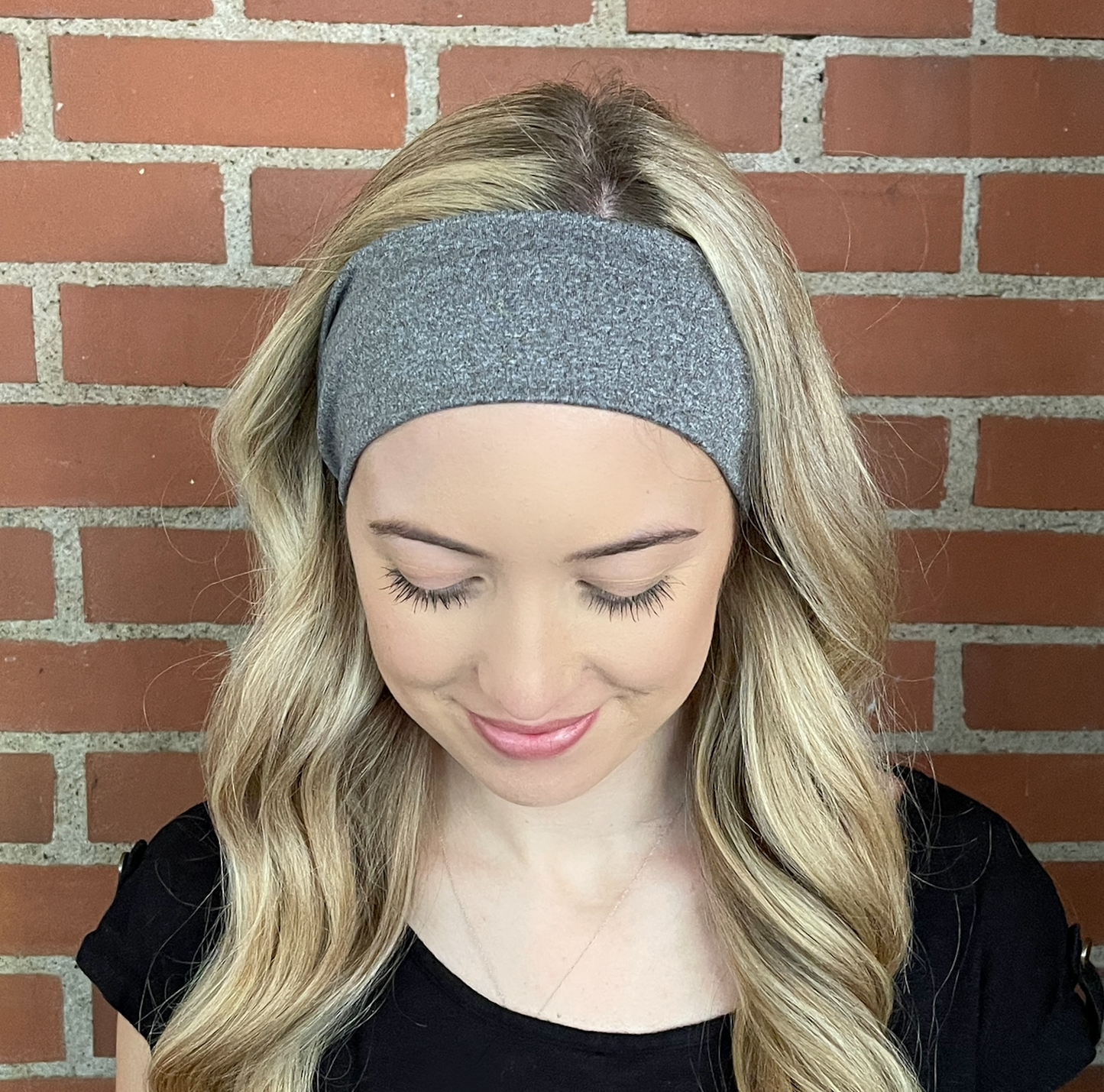 Woman with curled hair wearing flat, stretchy, heather gray headband.