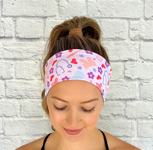 Woman with hair in ponytail wearing flat, stretchy, lavender color headband with medical, heart, and flower theme print.
