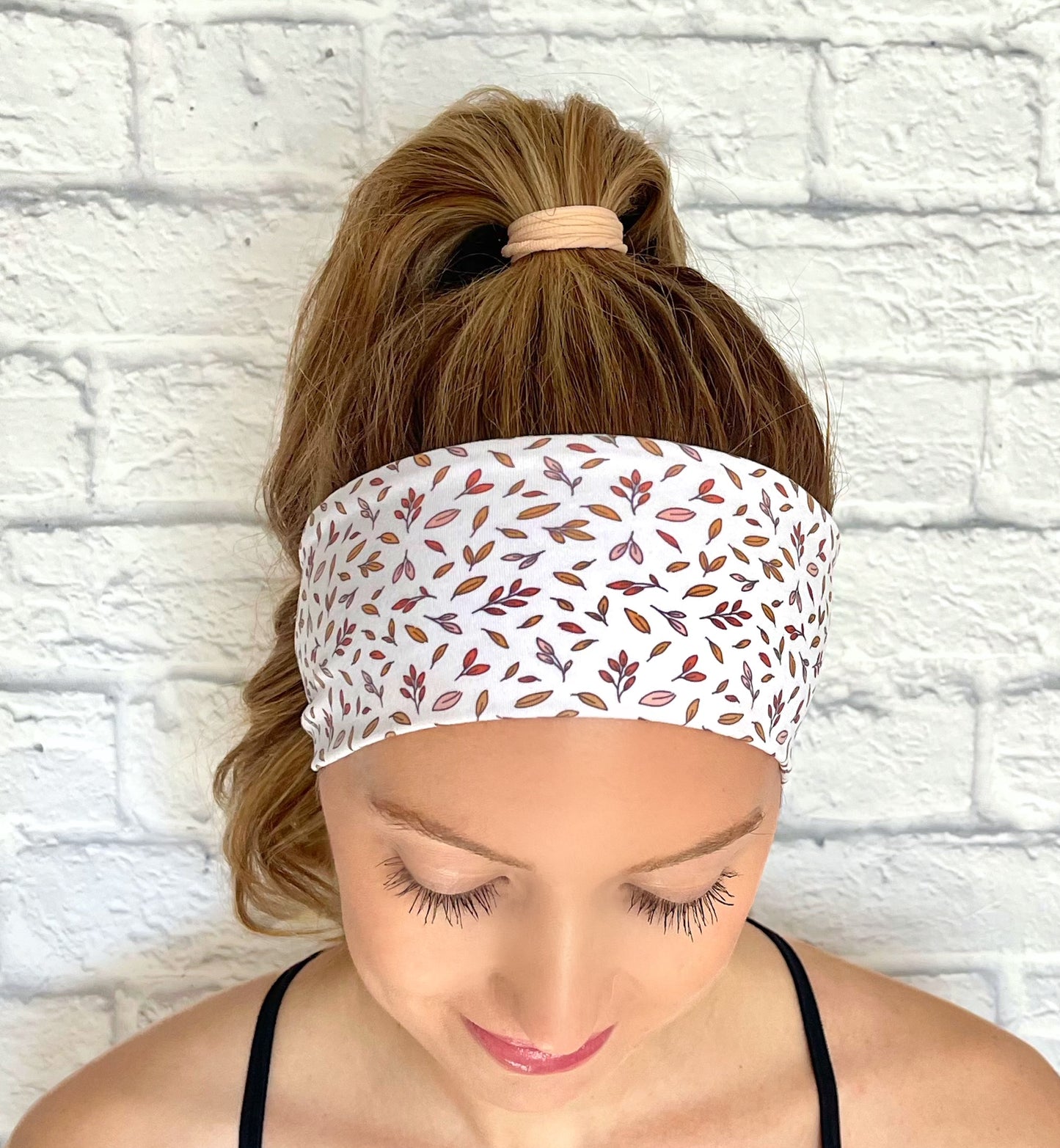 Woman with hair in curled ponytail wearing flat, stretchy, white headband with small leaves print.