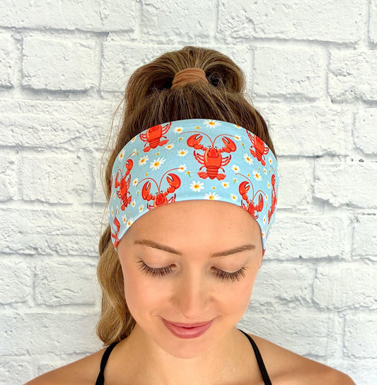 Woman wearing a headband with lobster pattern against a white brick wall.