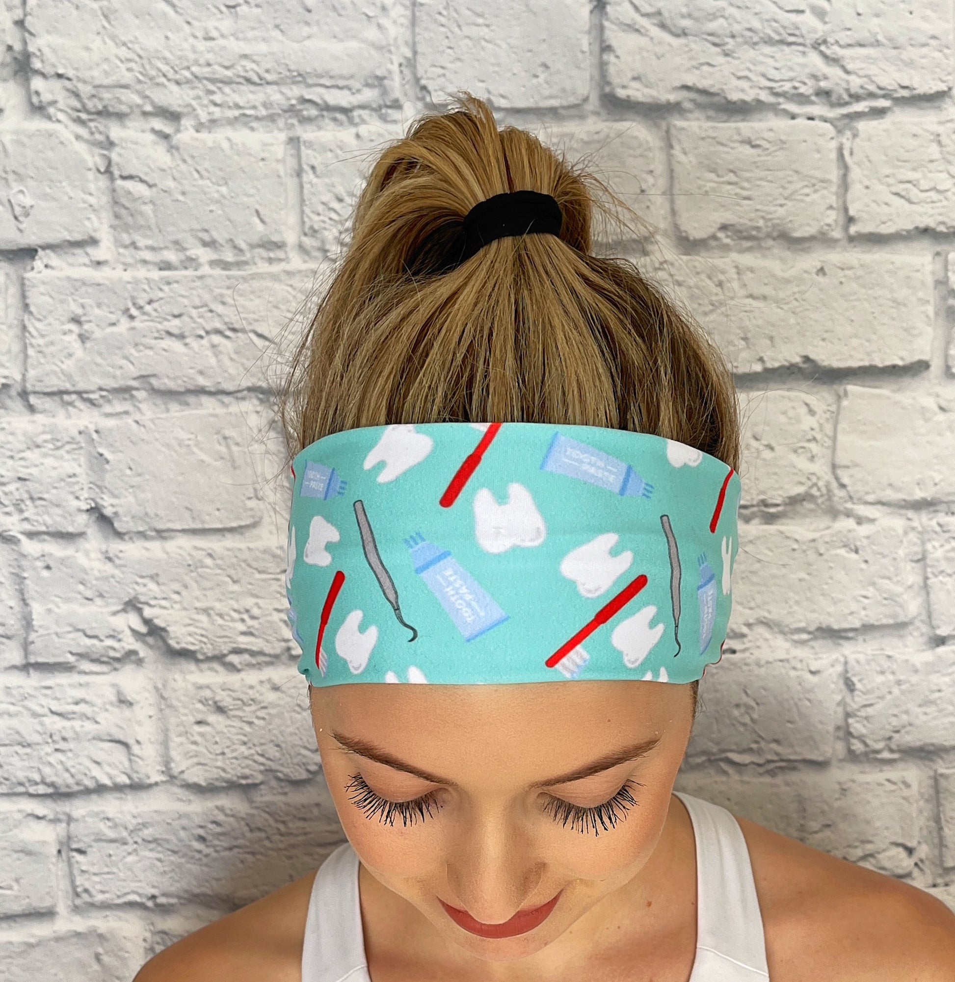 Woman with hair in ponytail wearing flat, stretchy headband in mint blue with dental theme print.