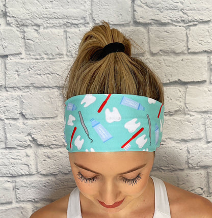 Woman with hair in ponytail wearing flat, stretchy headband in mint blue with dental theme print.