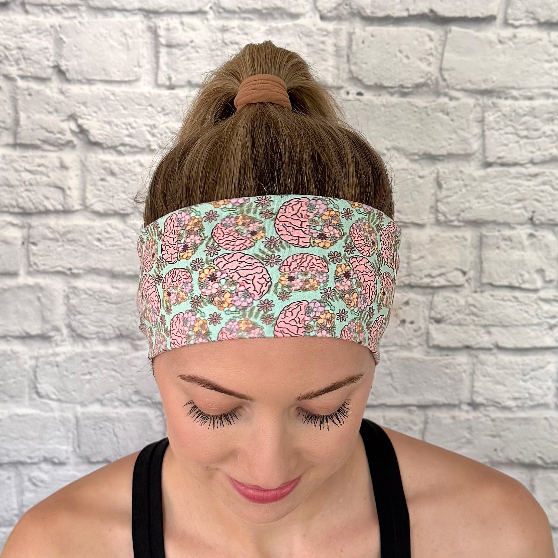 Woman with hair in bun wearing stretchy, mint green color headband with brain and floral print.