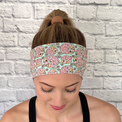 Woman with hair in bun wearing stretchy, mint green color headband with brain and floral print.