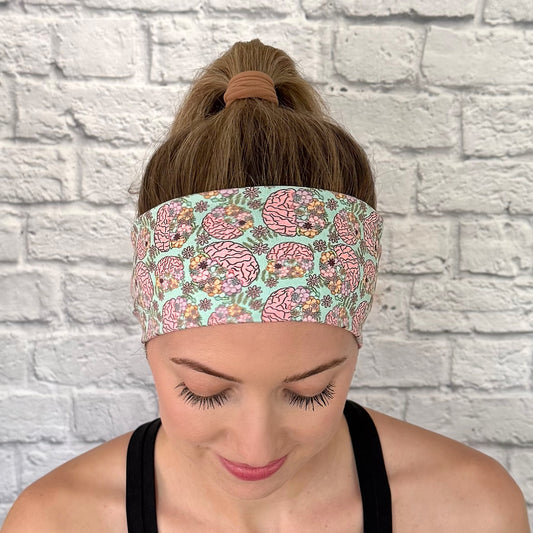 Woman with hair in bun wearing stretchy, mint green color headband with brain and floral print.