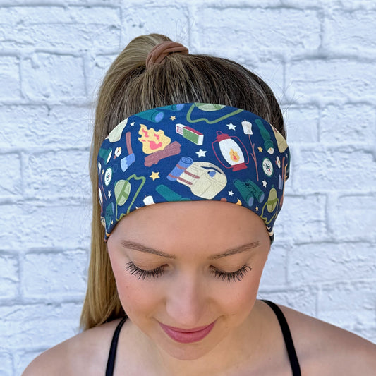 Woman with hair in ponytail weraing flat, stretchy, navy color headband with camping theme print.