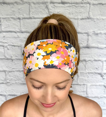Woman with hair in ponytail wearing headband with light and dark pink, navy, light blue, white, yellow, and orange flower print.
