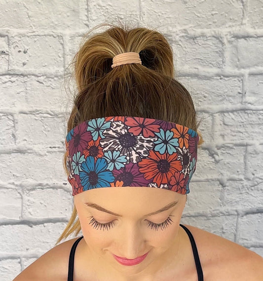 Woman wearing a navy floral headband against a light brick wall.