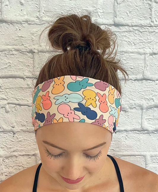 Woman with hair in bun wearing flat, stretchy headband in cream/peach color with pastel print Easter bunnies.