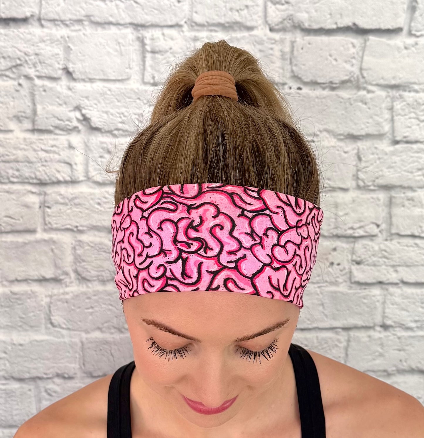 Woman with hair in ponytail wearing pink headband with pink/black brain print.