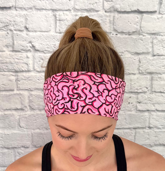 Woman with hair in ponytail wearing pink headband with pink/black brain print.