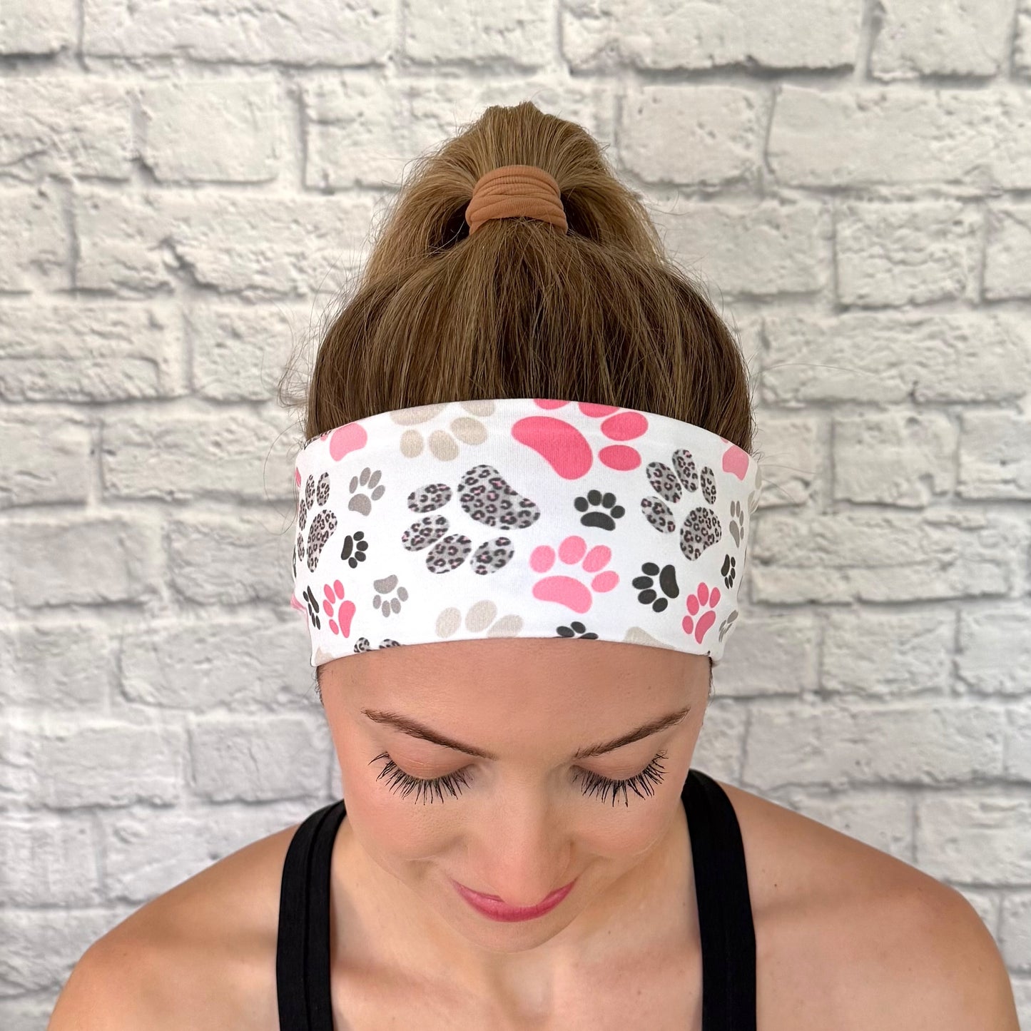Woman with hair in bun wearing flat, stretchy headband in white with pink, gray, and black paw print.