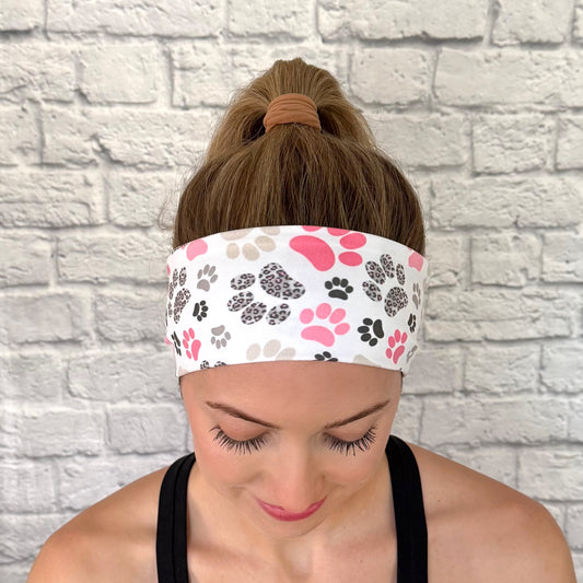 Woman with hair in bun wearing flat, stretchy headband in white with pink, gray, and black paw print.