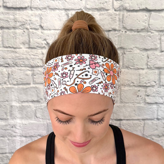 Woman wearing white headband with orange and pink medical theme print. Contains hearts, flowers, stethoscopes, bandages, and syringes.