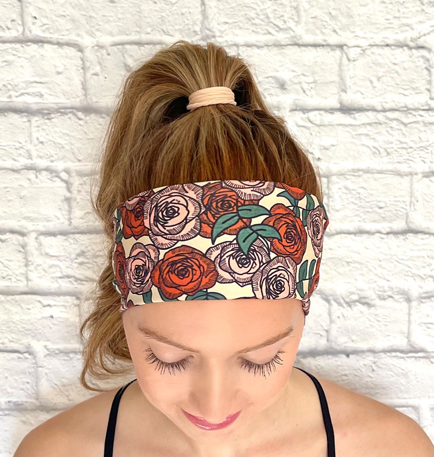 Woman with hair in curled ponytail wearing flat, stretchy headband with rose print.