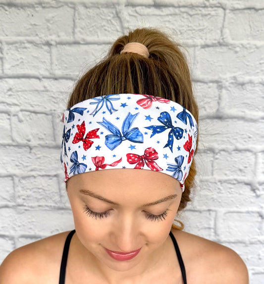 Flat, stretchy, white headband with red and blue bow print and blue stars.
