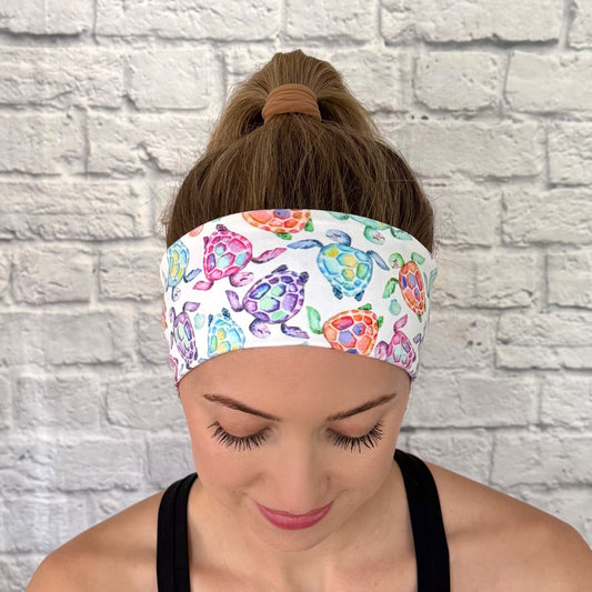 Woman with hair in ponytail wearing a flat, stretchy, white headband with sea turtle print.