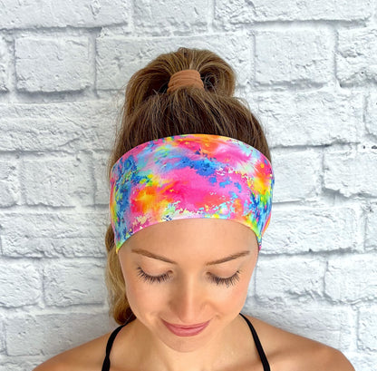 Woman wearing flat, stretchy headband in rainbow color paint-splatter looking print.
