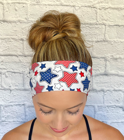 Woman wearing a headband with red, white, and blue star pattern headband against a white brick wall.