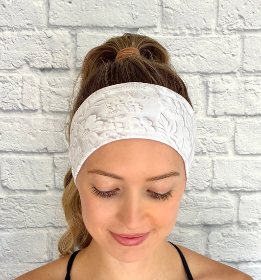 Woman with hair in ponytail wearing flat, stretchy, white headband with faux embossed floral print and gray shadowing.
