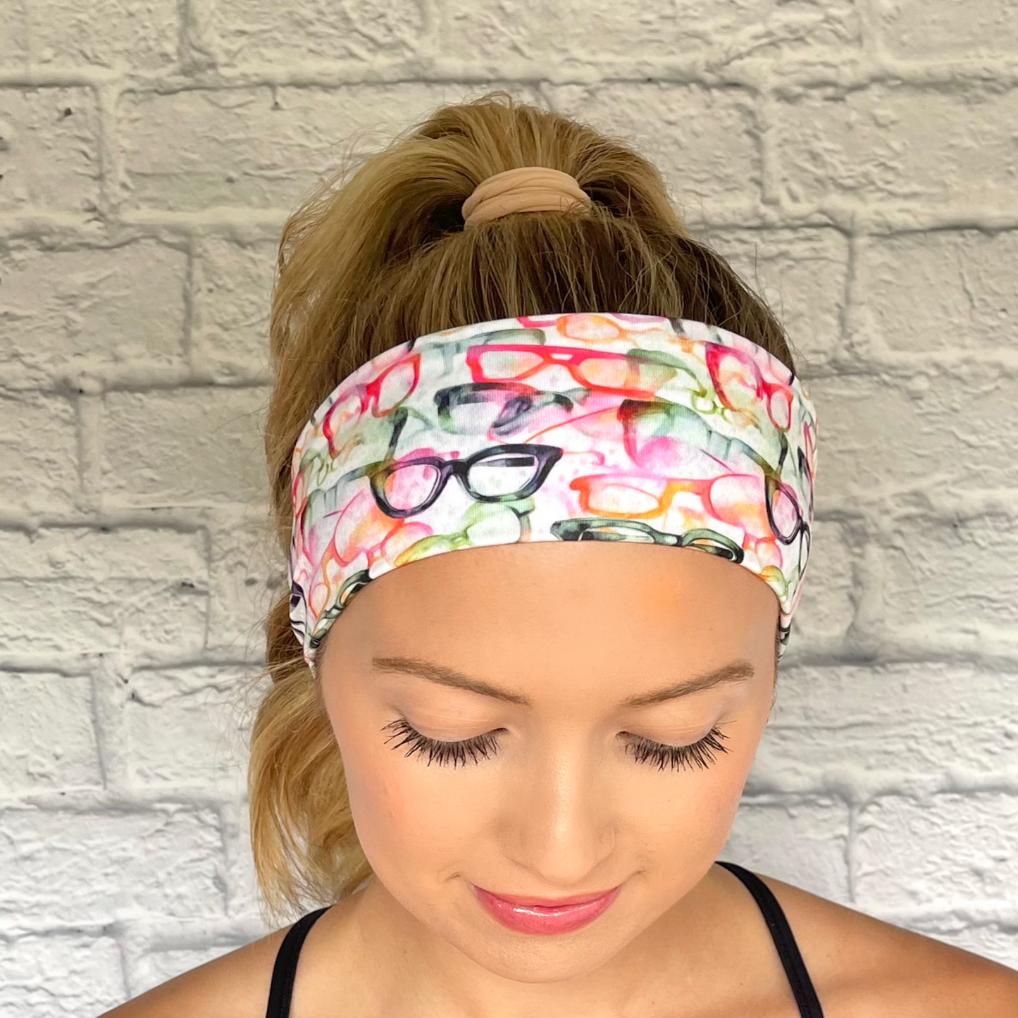 Woman with hair in ponytail wearing white headband with rainbow color eye glasses print.