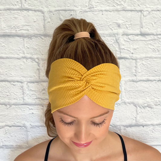 Woman with hair in curled ponytail wearing wide, ribbed, twisted, gold color headband.