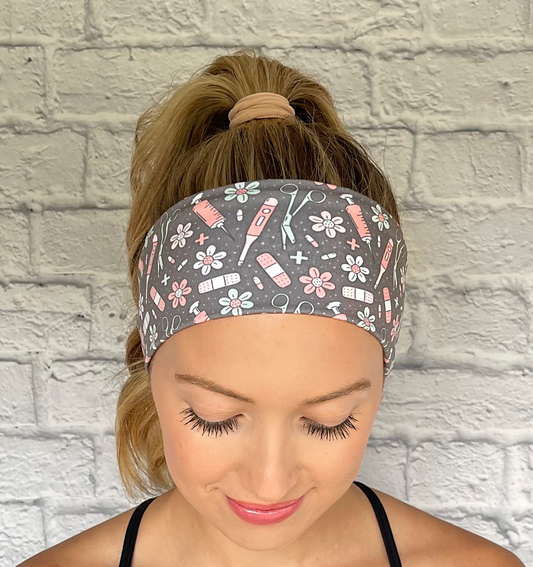 Woman with hair in curled ponytail wearing stretchy, gray headband with pink, white, and seafoam green medical and floral theme print.