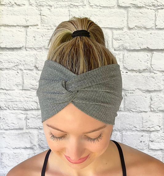 Woman with hair in ponytail wearing wide, twisted headband in gray ribbed fabric.