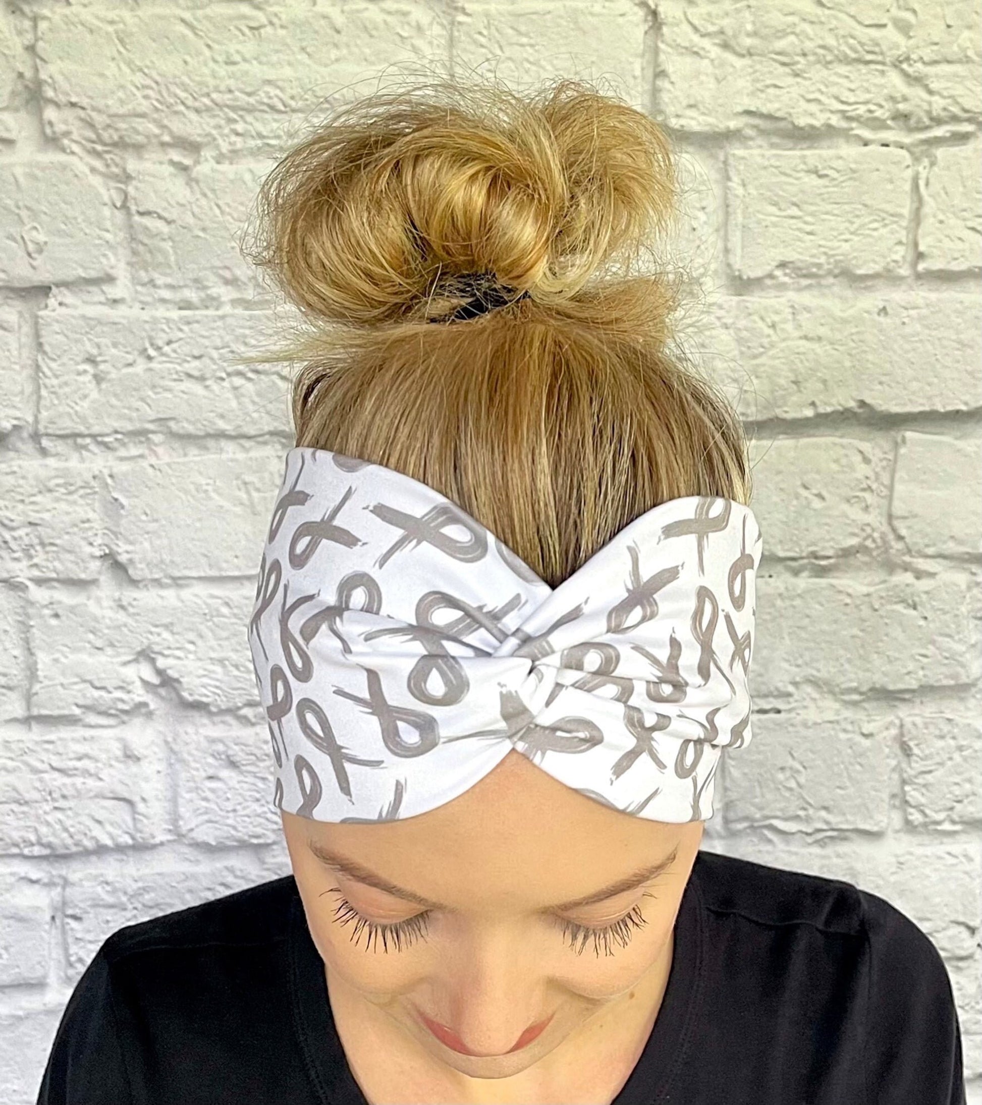 Woman with hair in bun wearing white, wide twist headband with gray ribbons.